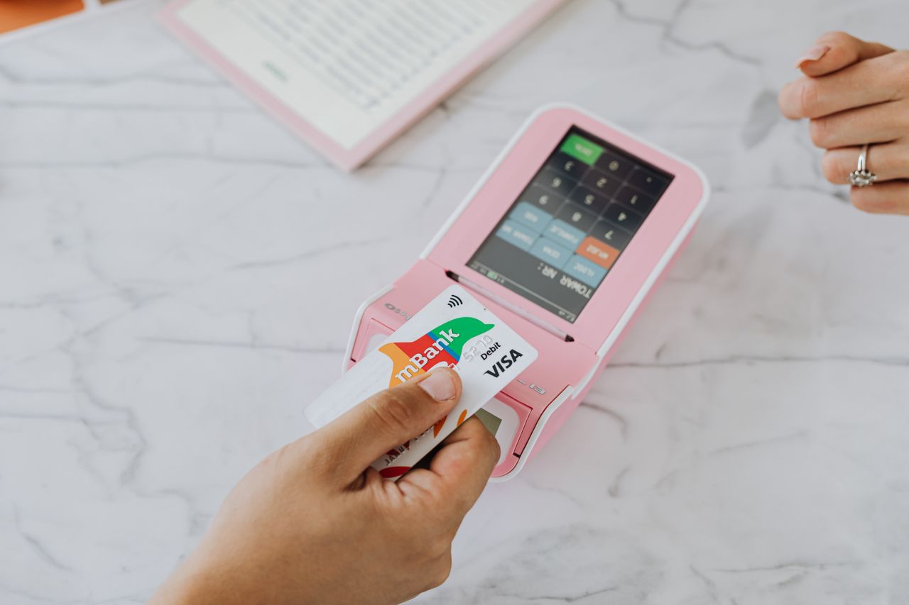 hero-img-02 Main utilisant une carte sans contact sur un terminal POS rose pour une transaction sans fil.